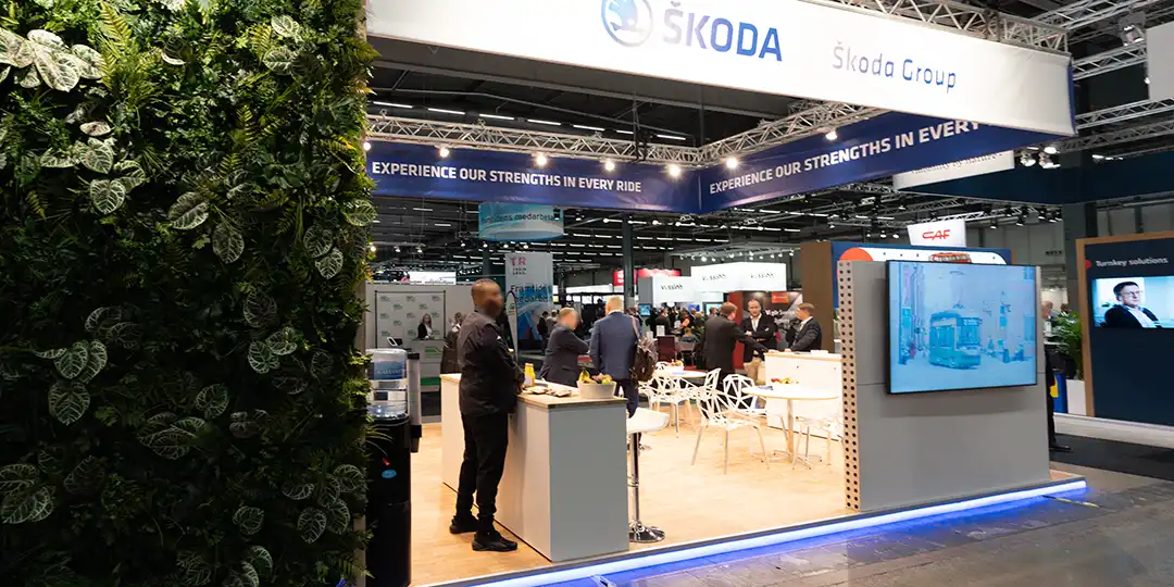 puff_eventservice Škoda Group stand at a trade fair with visitors in conversation and a screen showing a presentation.